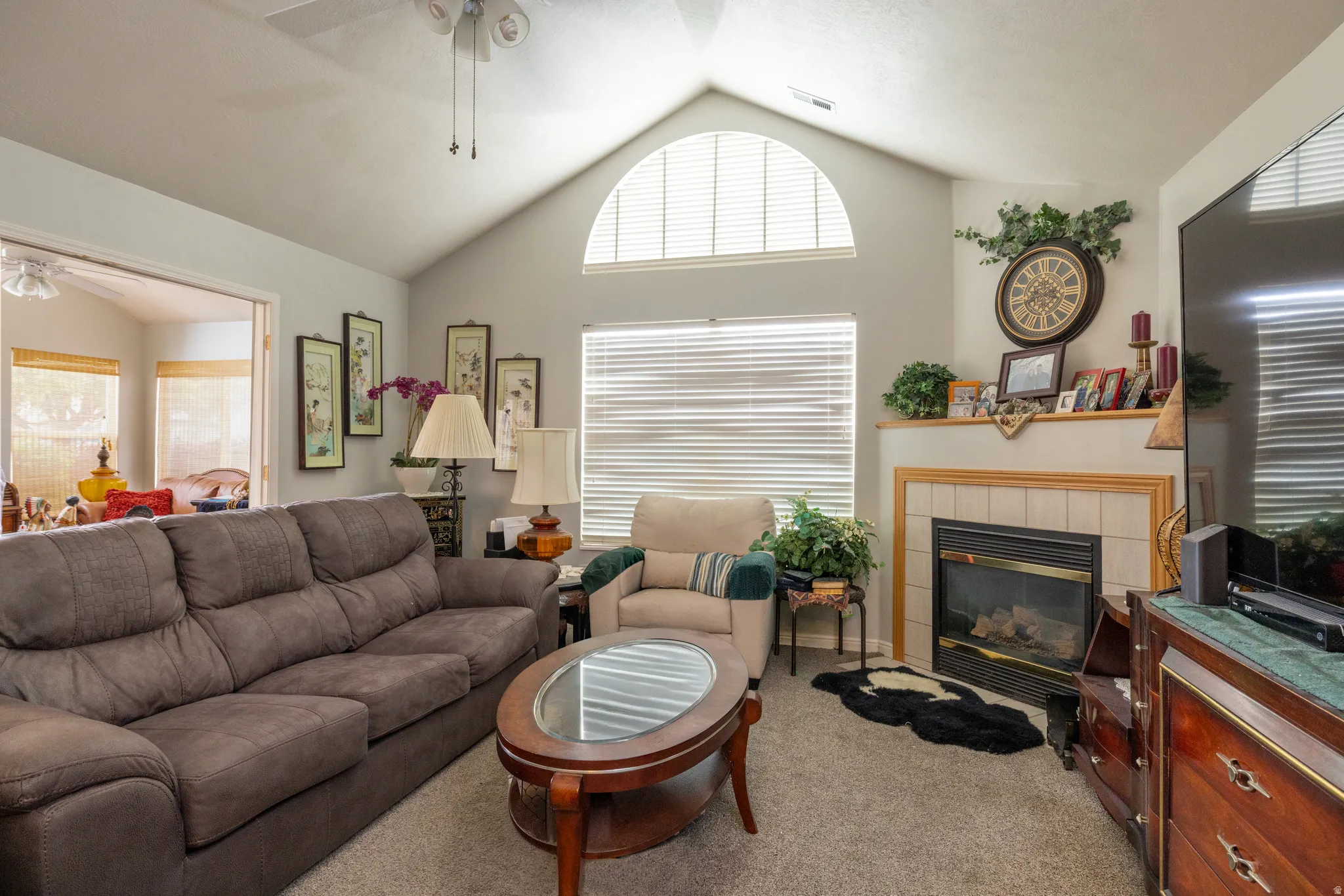 Living area with a ceiling fan, light carpet, a tile fireplace, and a high ceiling