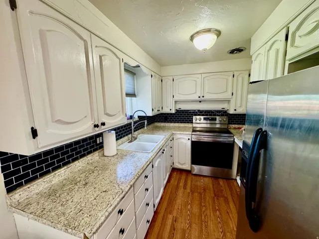 Kitchen featuring stainless steel appliances, tasteful backsplash, white cabinets, dark wood-type flooring, and light stone counters