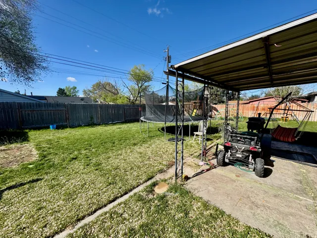 Fenced backyard featuring a trampoline and a patio