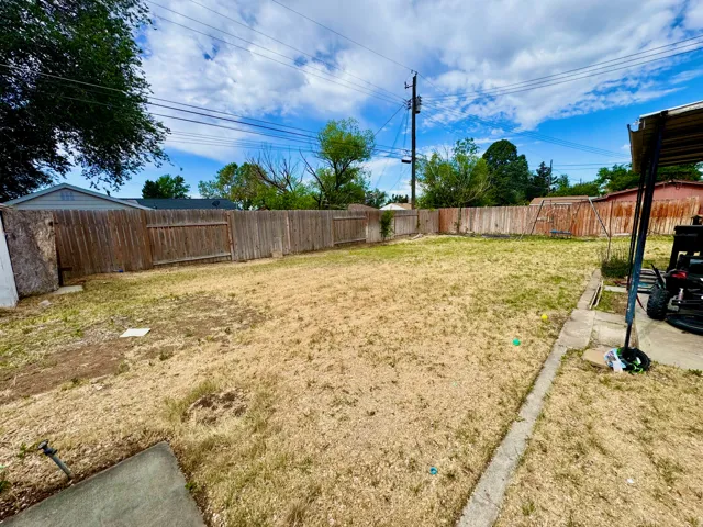 Expansive backyard featuring a full perimeter wood privacy fence, concrete patio area, and mature trees providing partial shade
