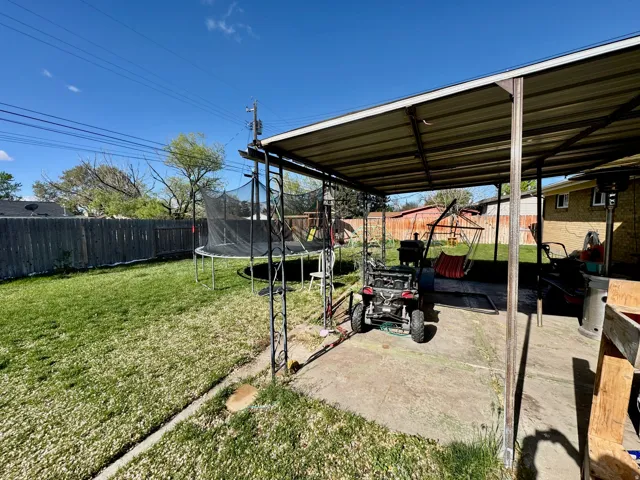 Fenced backyard featuring a trampoline and a patio