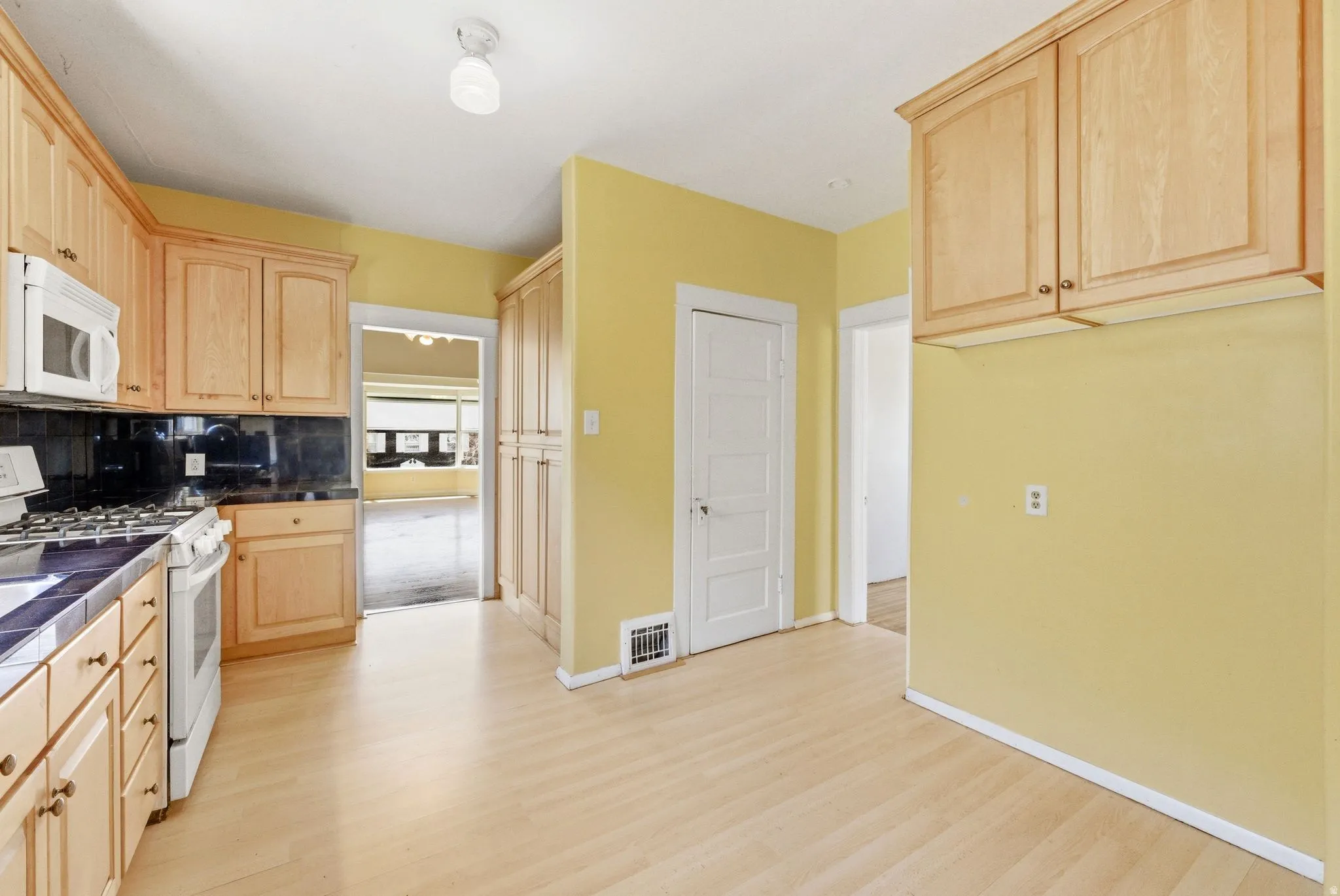 Kitchen with light wood finish cabinetry, dark countertops, white appliances, tasteful backsplash, and light wood finished floors