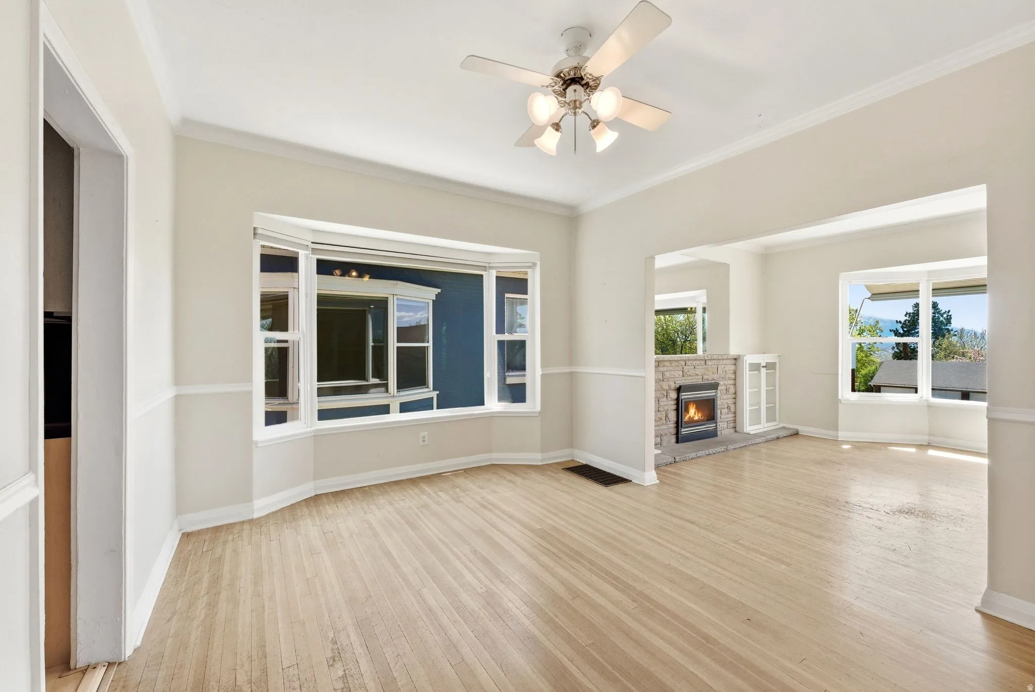 Unfurnished living room with light wood finished floors, a ceiling fan, ornamental molding, and a fireplace