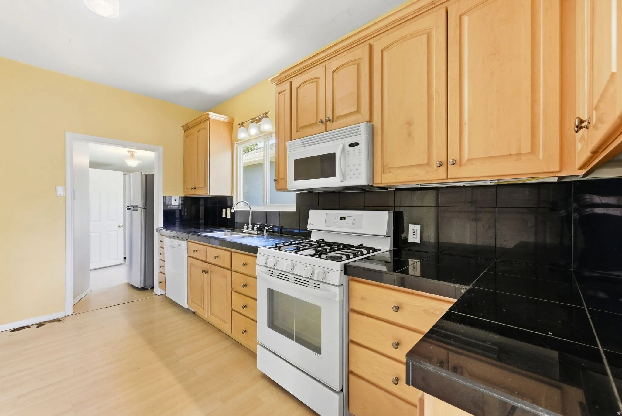 Kitchen with light wood finish cabinets, white appliances, decorative backsplash, and light wood-style floors