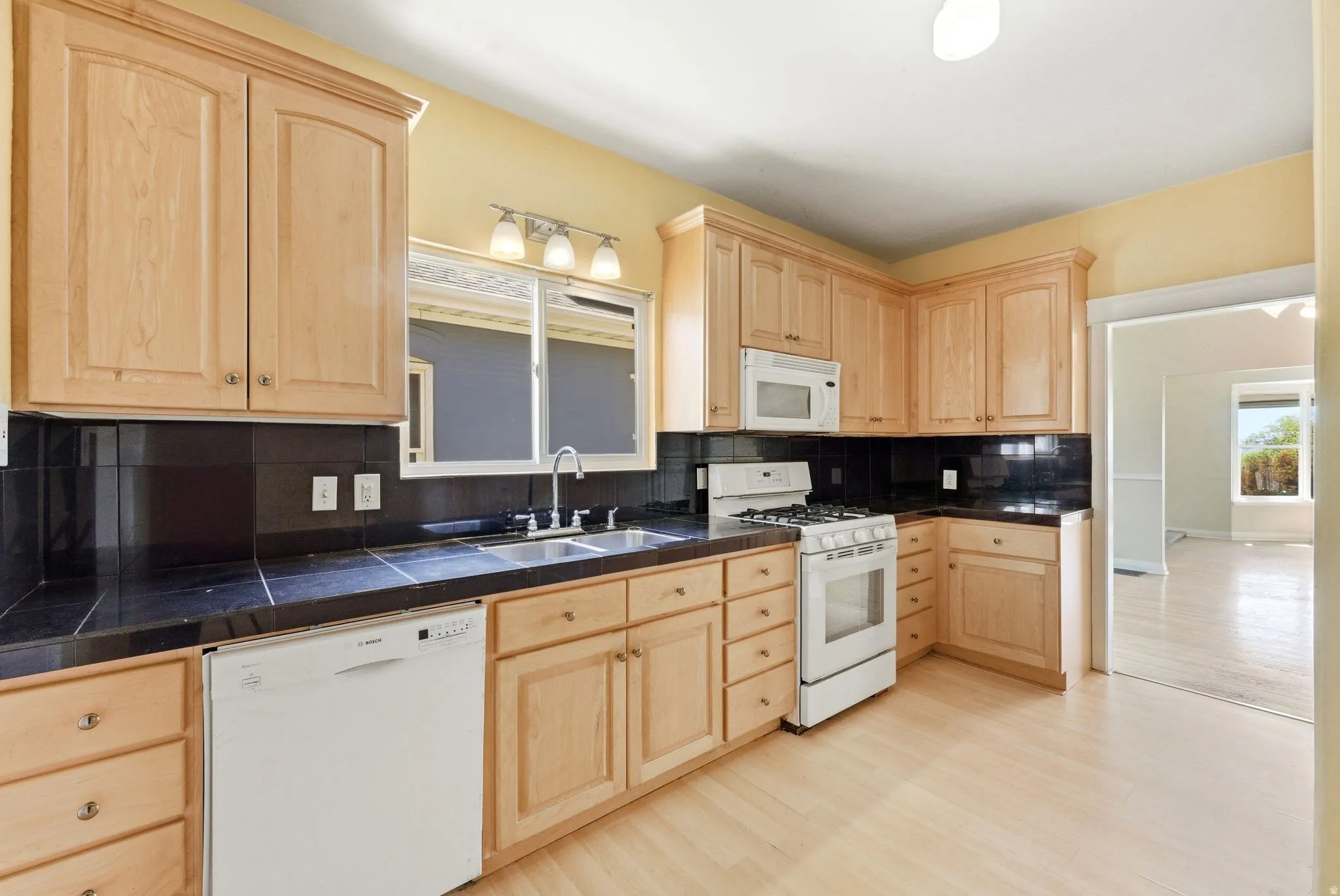 Kitchen with light wood finish cabinets, white appliances, tasteful backsplash, and light wood-style floors