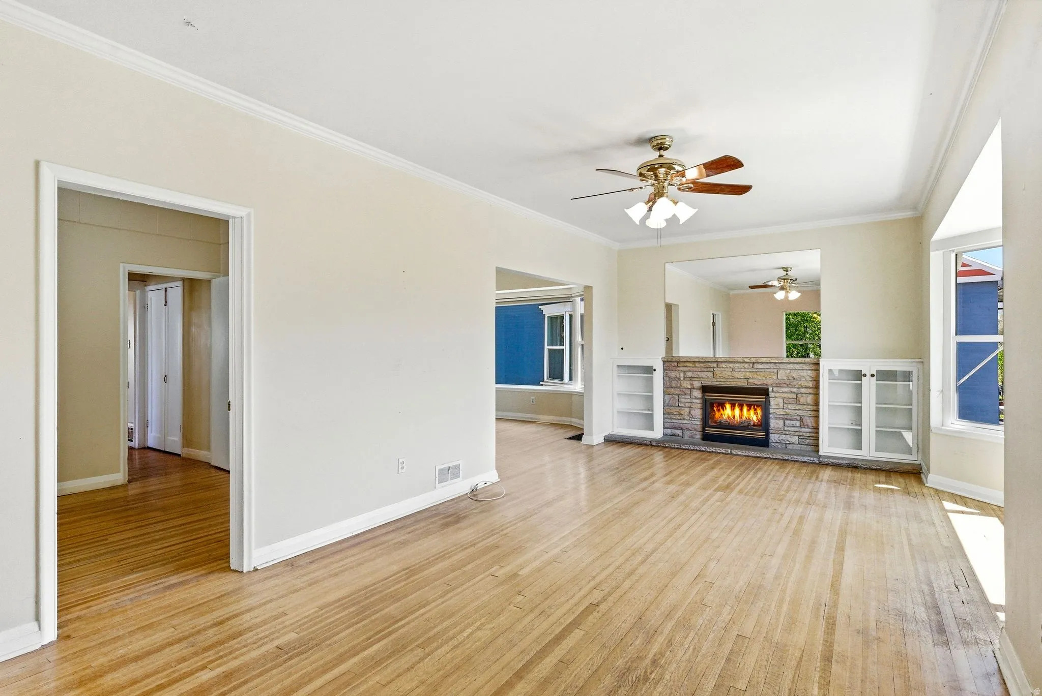 Unfurnished living room featuring a fireplace, light wood-type flooring, ceiling fan, and ornamental molding