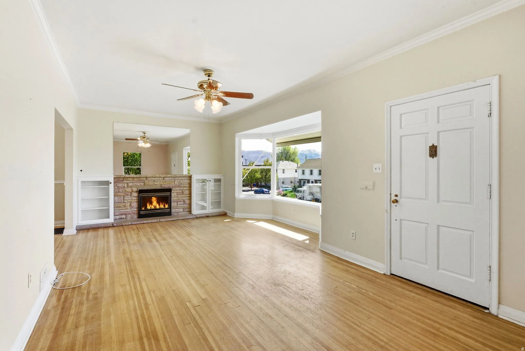 Unfurnished living room featuring a fireplace, ceiling fan, light wood-style flooring, and crown molding