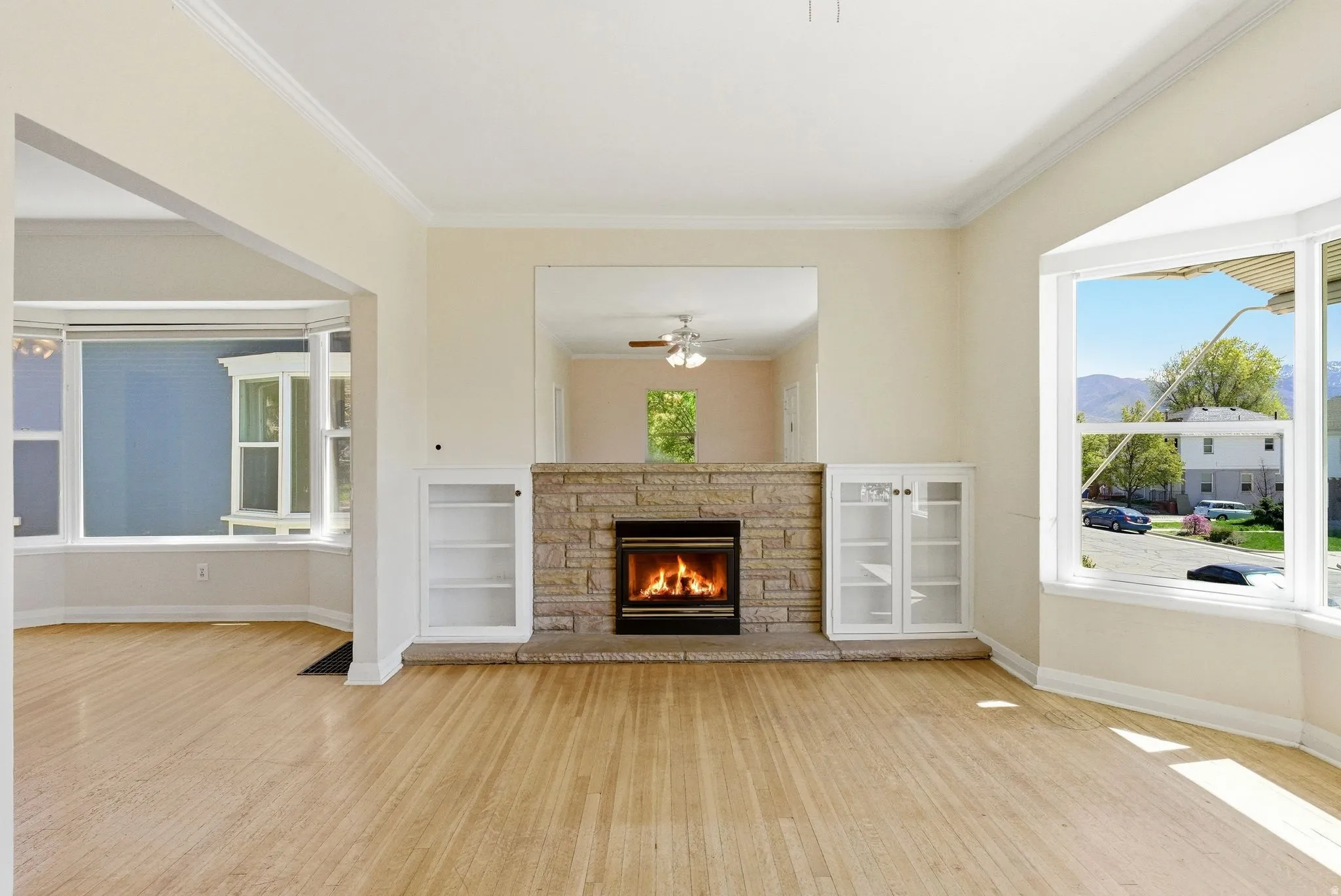 Unfurnished living room with a fireplace, light wood-style flooring, crown molding, ceiling fan, and a mountain view