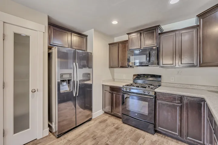 Kitchen featuring black appliances, dark wood finish cabinetry, light countertops, light wood-type flooring, and recessed lighting