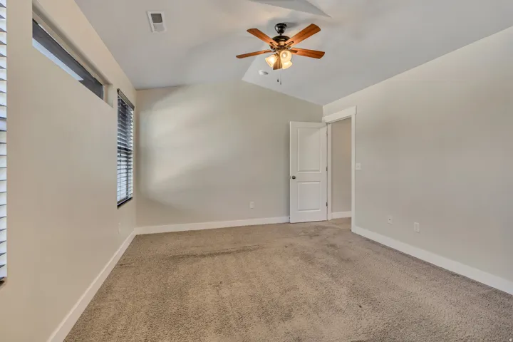 Empty room featuring a ceiling fan, light carpet, and lofted ceiling