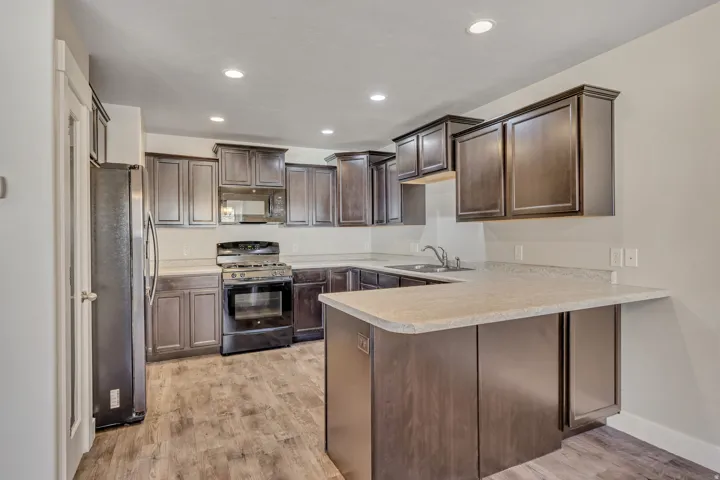 Kitchen featuring dark wood finish cabinets, black appliances, a peninsula, light wood-style floors, and light countertops