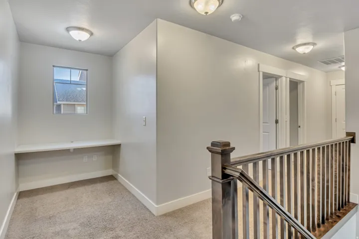 Hallway with an upstairs landing and light colored carpet