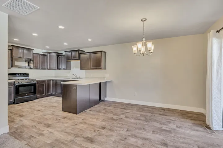 Kitchen with dark wood finish cabinets, stainless steel range with gas stovetop, a peninsula, light countertops, and black microwave