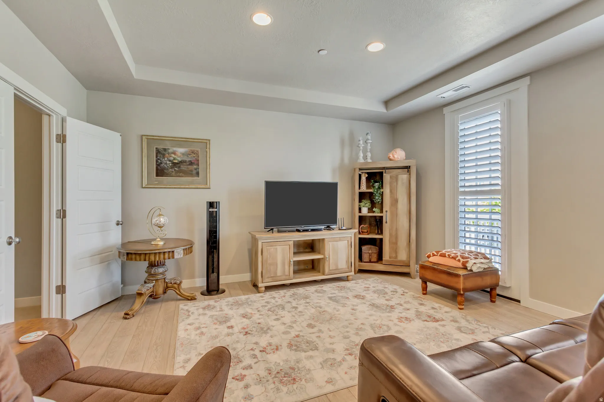 Living area with a raised ceiling, light wood-type flooring, and recessed lighting
