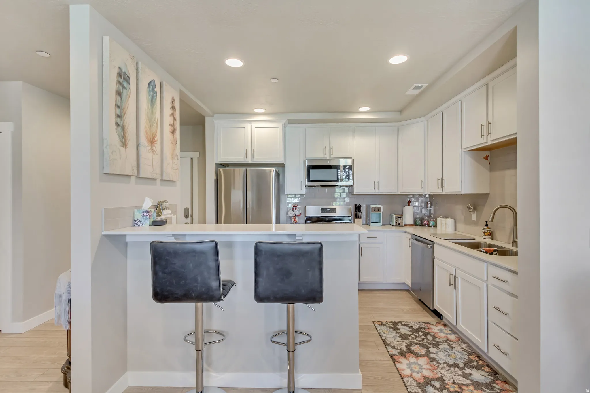 Kitchen featuring white cabinets, a kitchen bar, light wood-type flooring, stainless steel appliances, and recessed lighting