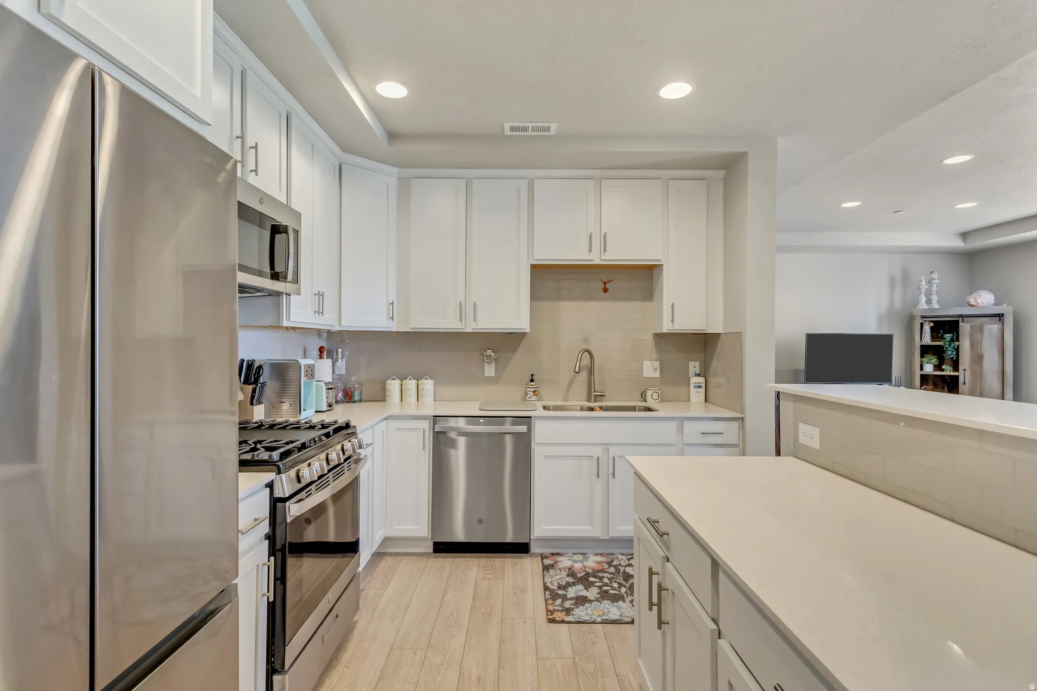 Kitchen with stainless steel appliances, white cabinetry, recessed lighting, light wood-type flooring, and light stone counters