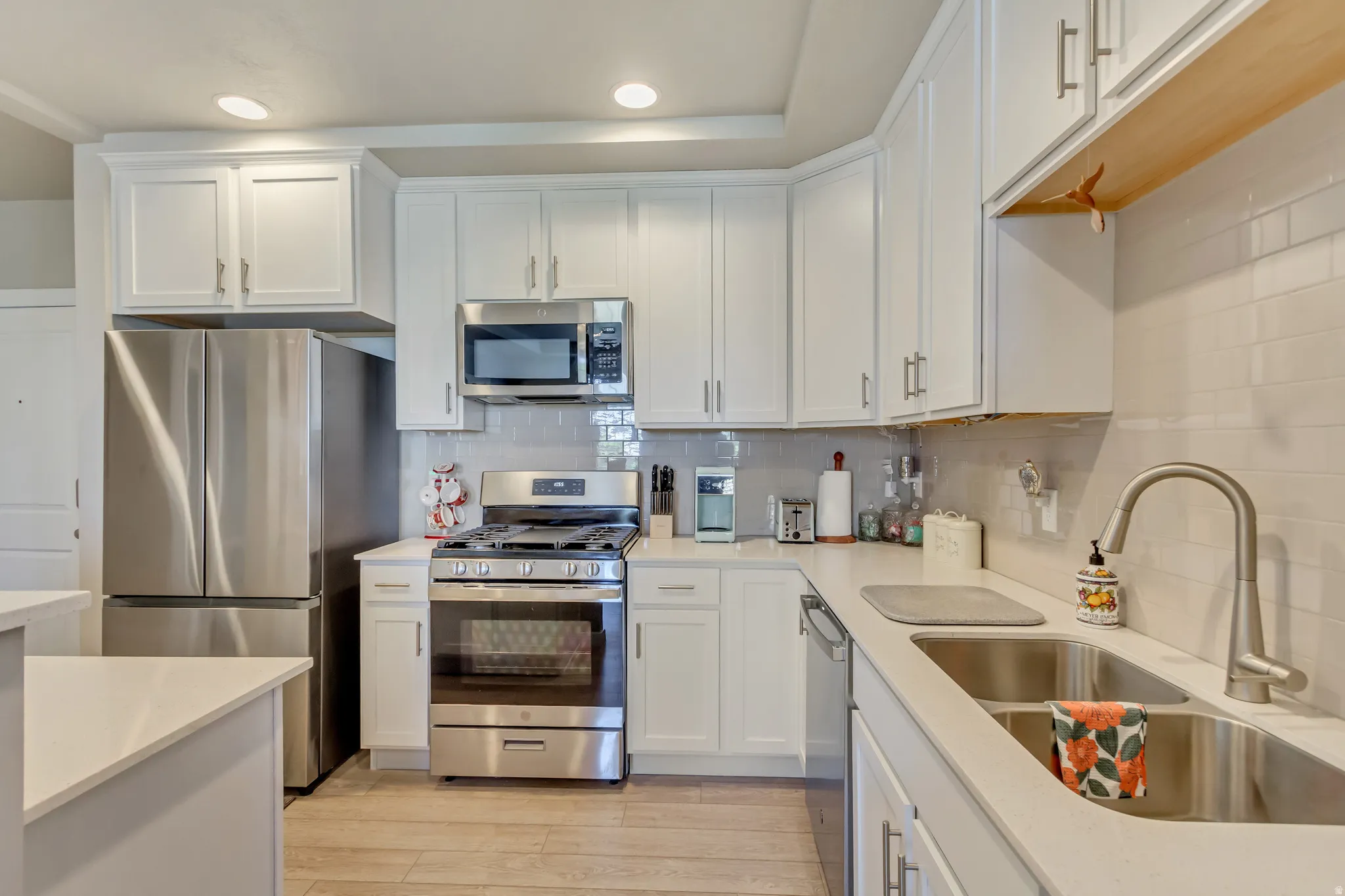 Kitchen featuring stainless steel appliances, white cabinets, light wood finished floors, decorative backsplash, and recessed lighting