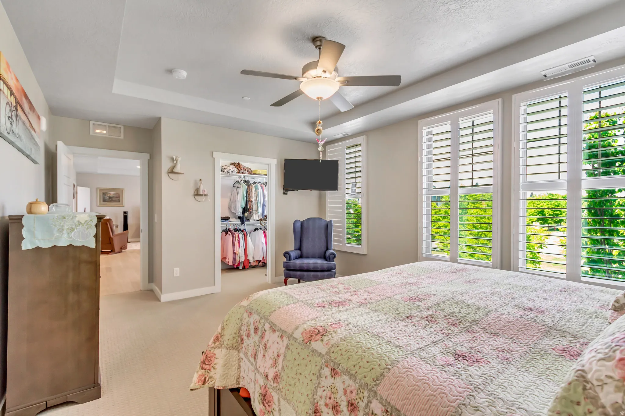 Bedroom with a raised ceiling, a walk in closet, light colored carpet, and ceiling fan