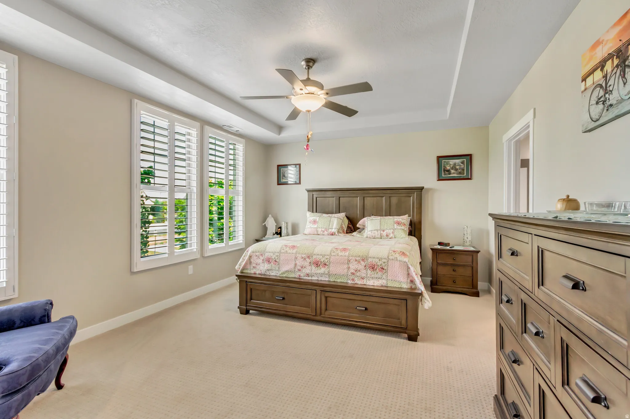 Bedroom featuring a raised ceiling, light colored carpet, and ceiling fan