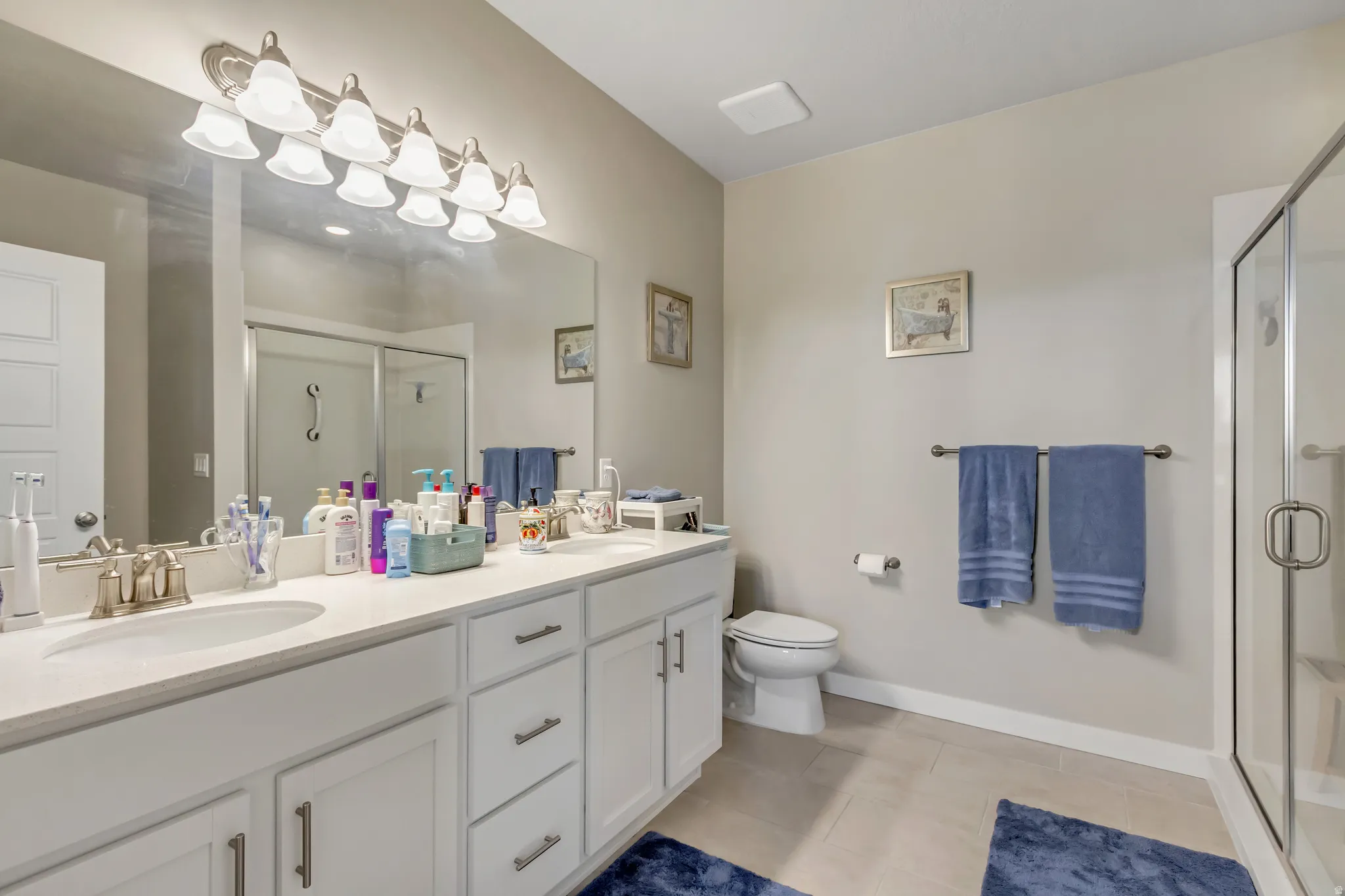 Full bathroom with a shower stall, double vanity, and light tile patterned floors