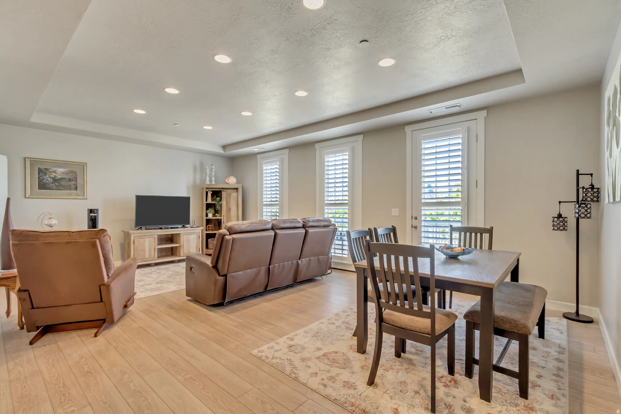 Dining space with a raised ceiling, recessed lighting, light wood-style flooring, and a textured ceiling