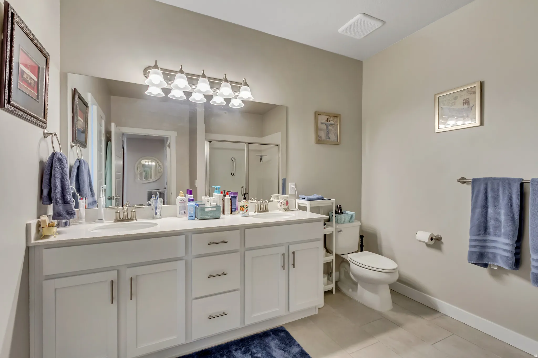 Bathroom featuring double vanity, a stall shower, and light tile patterned floors