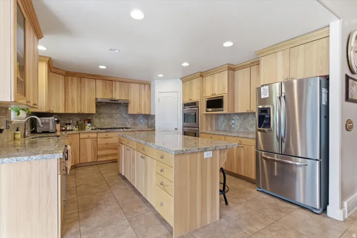 Kitchen featuring light wood finish cabinets, stainless steel appliances, light stone counters, light tile patterned floors, and recessed lighting