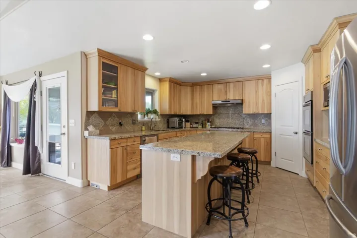 Kitchen featuring light stone countertops, a kitchen breakfast bar, stainless steel appliances, a center island, and glass insert cabinets