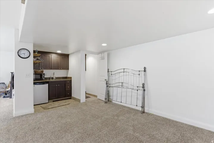 Indoor wet bar featuring dark wood finish cabinetry, light carpet, recessed lighting, black microwave, and fridge