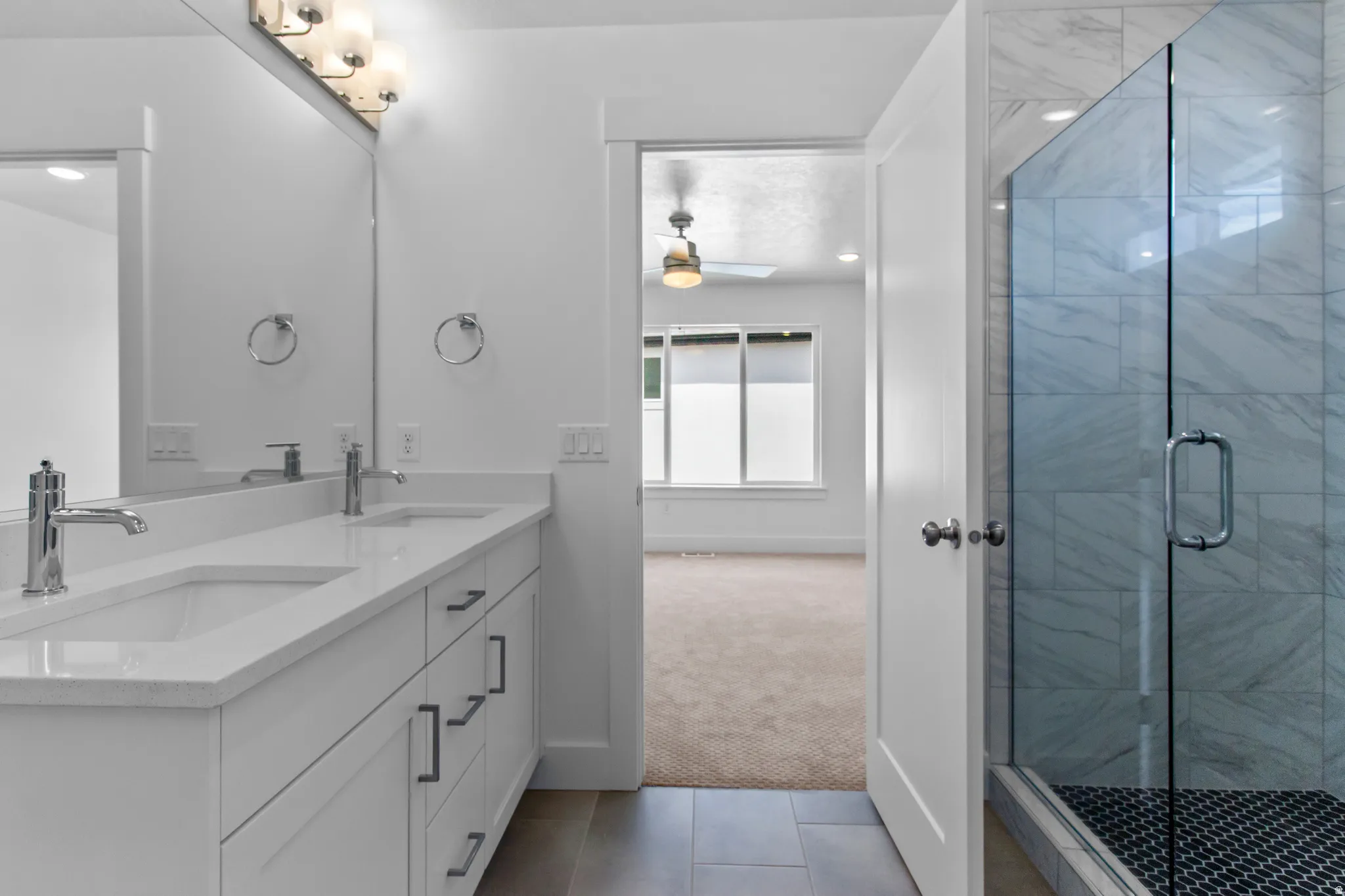 Bathroom featuring double vanity, a stall shower, light tile patterned floors, light colored carpet, and ceiling fan