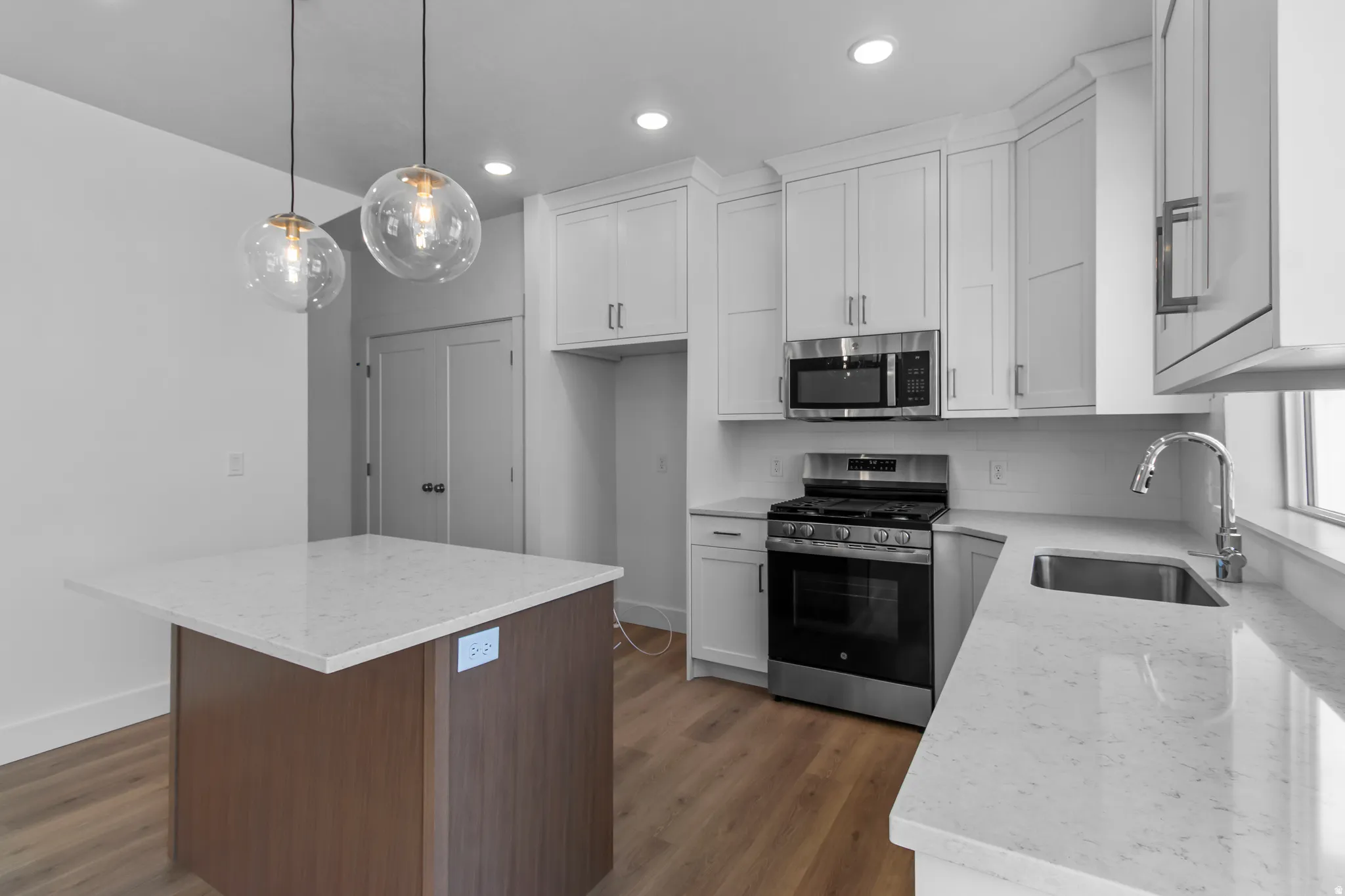 Kitchen featuring light stone counters, stainless steel appliances, a kitchen island, hanging light fixtures, and dual tone cabinets