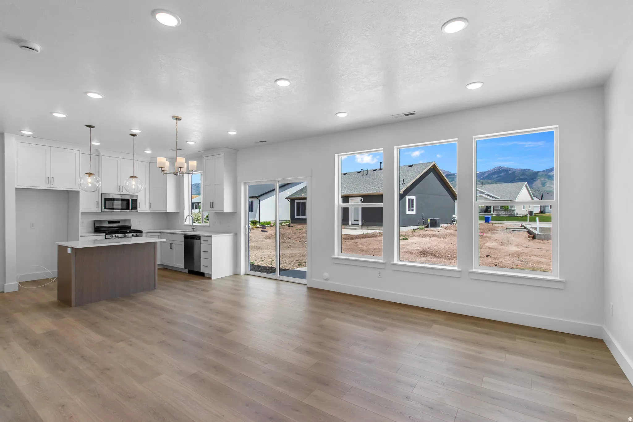 Two tone kitchen featuring a center island, open floor plan, two tone cabinetry, stainless steel appliances, and hanging lights