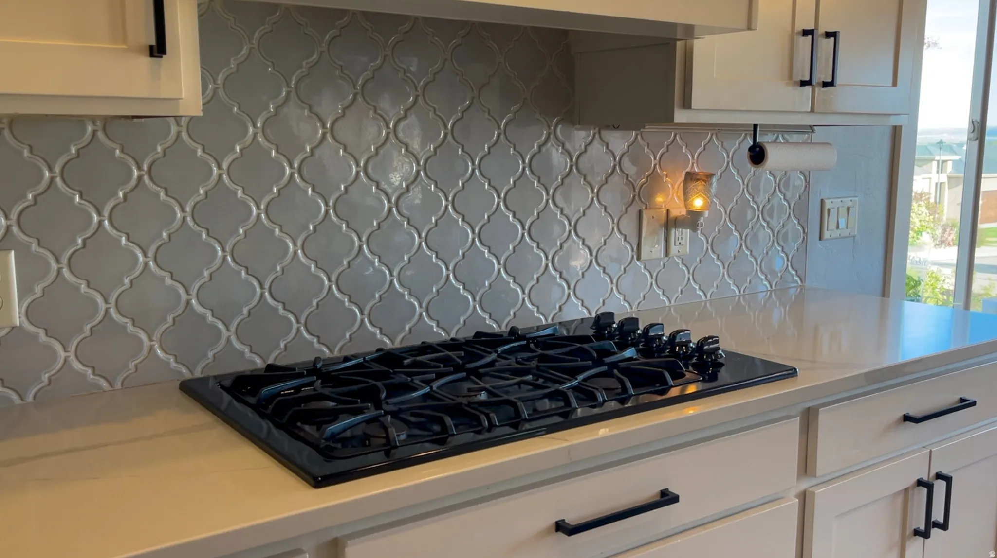 Kitchen with black gas cooktop, white cabinets, tasteful backsplash, and light stone counters