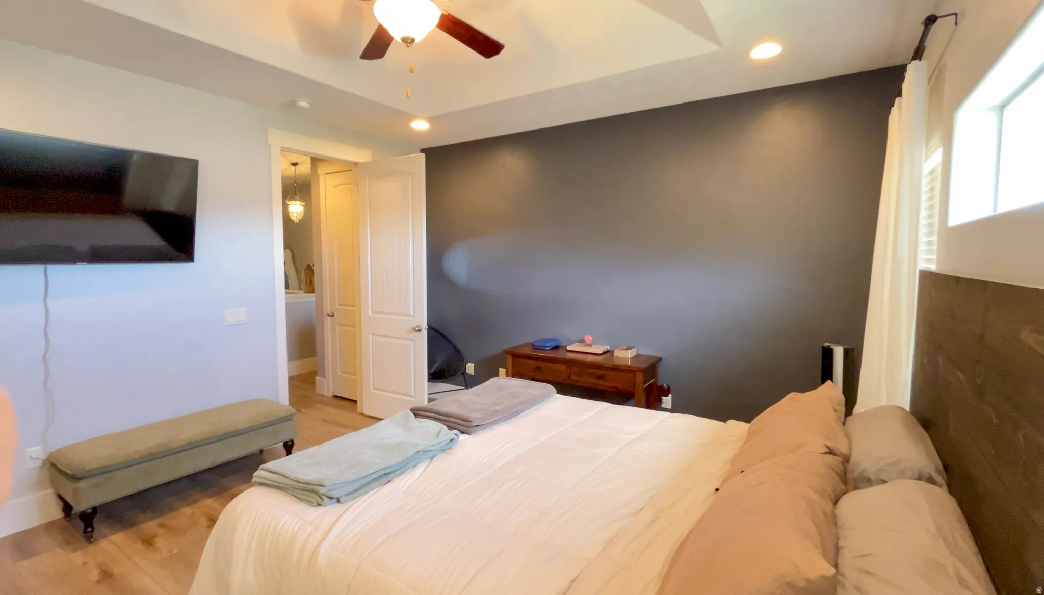 Bedroom with light wood-style flooring, a raised ceiling, recessed lighting, and a ceiling fan