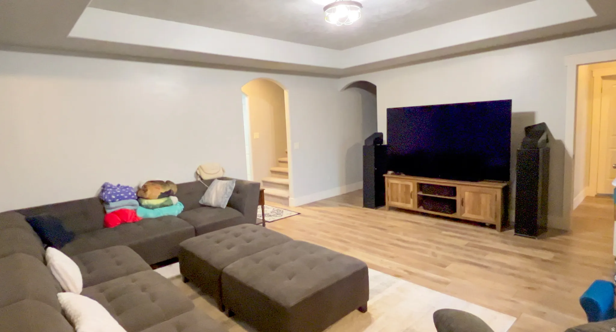 Living room with a tray ceiling, light wood-style floors, and arched walkways