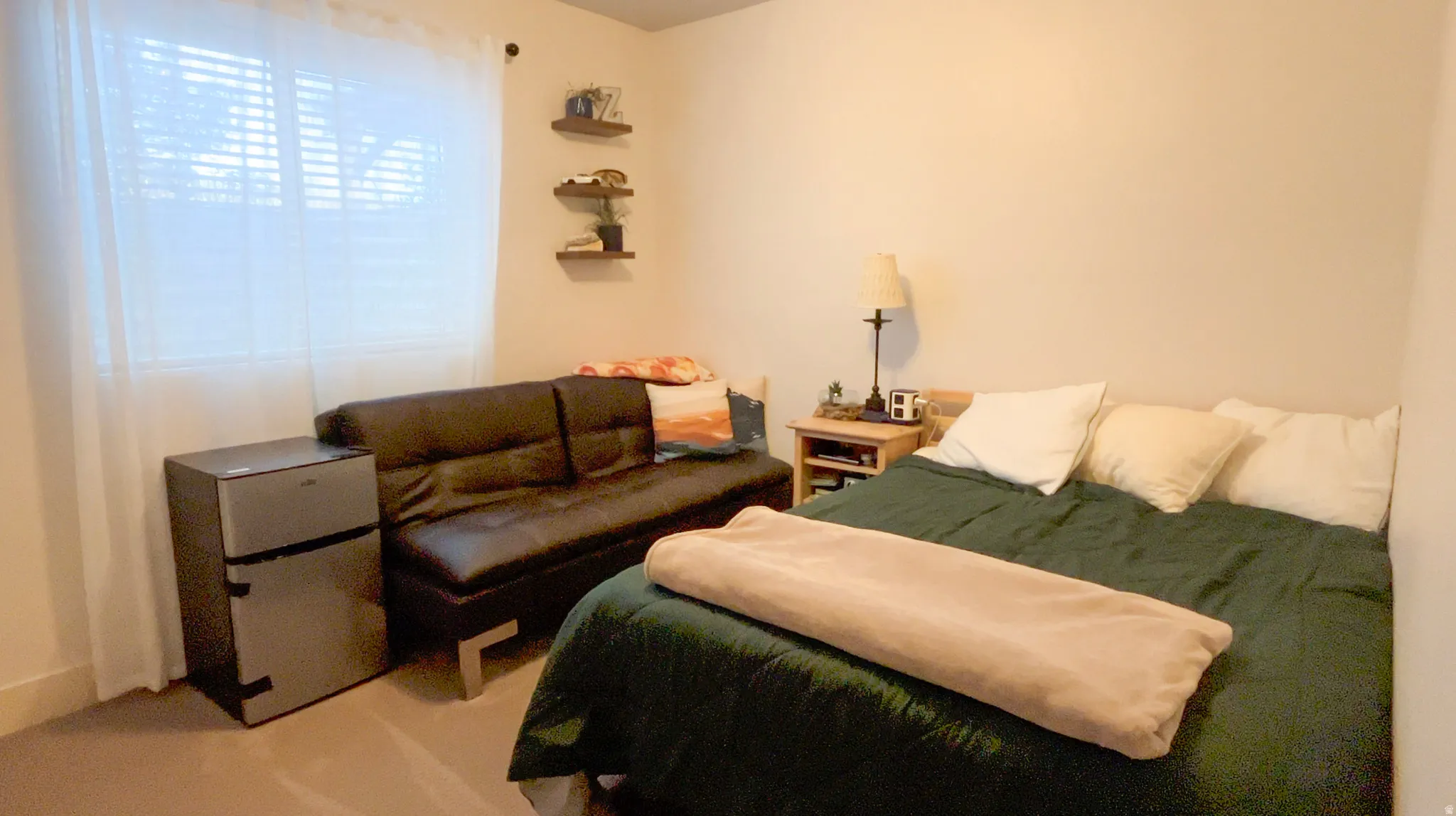 Bedroom with freestanding refrigerator and light colored carpet