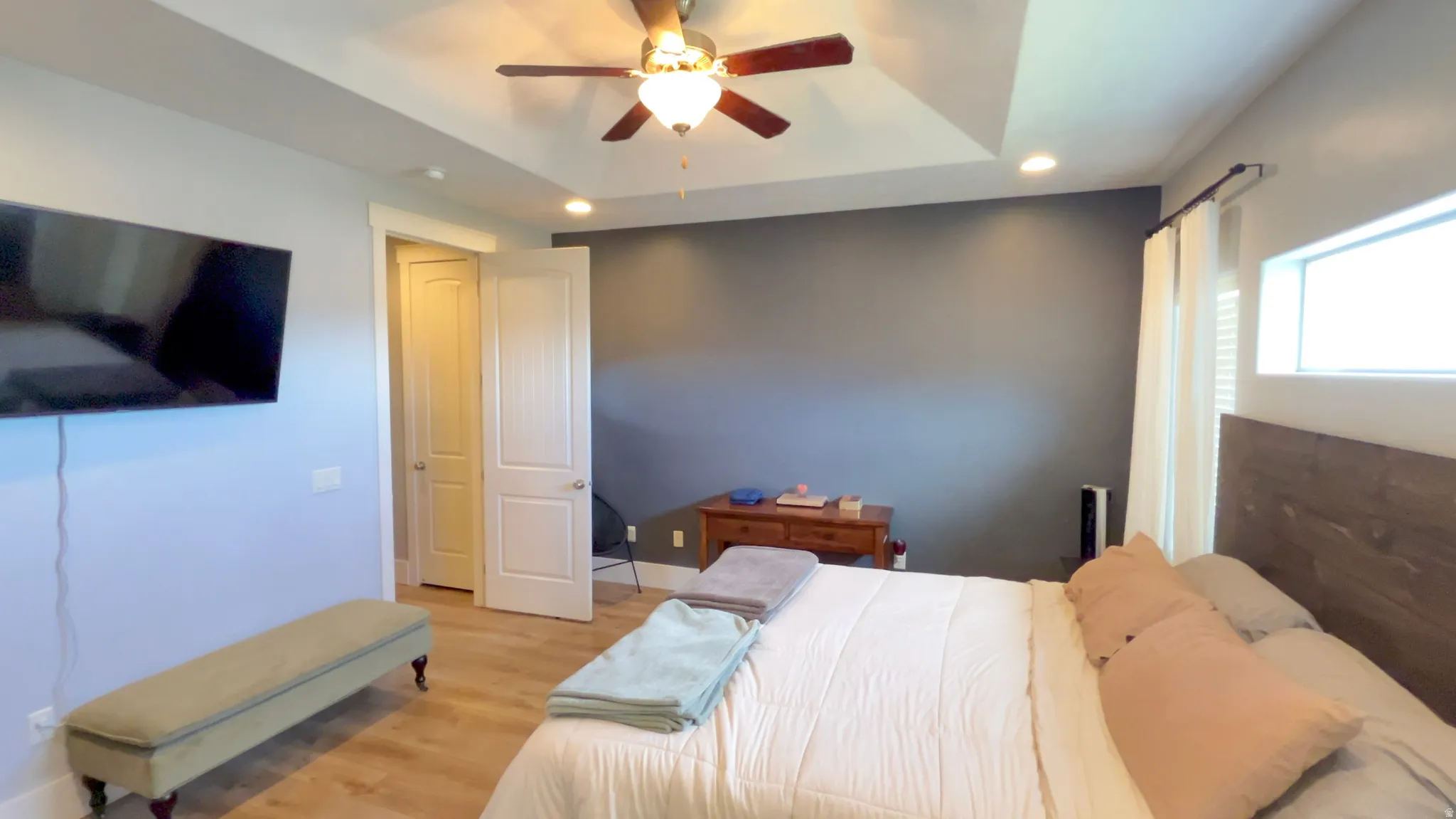 Bedroom featuring light wood finished floors, a raised ceiling, recessed lighting, and ceiling fan