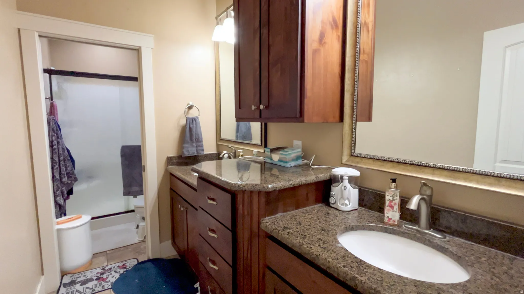 Full bath featuring two vanities, a shower stall, and light tile patterned floors
