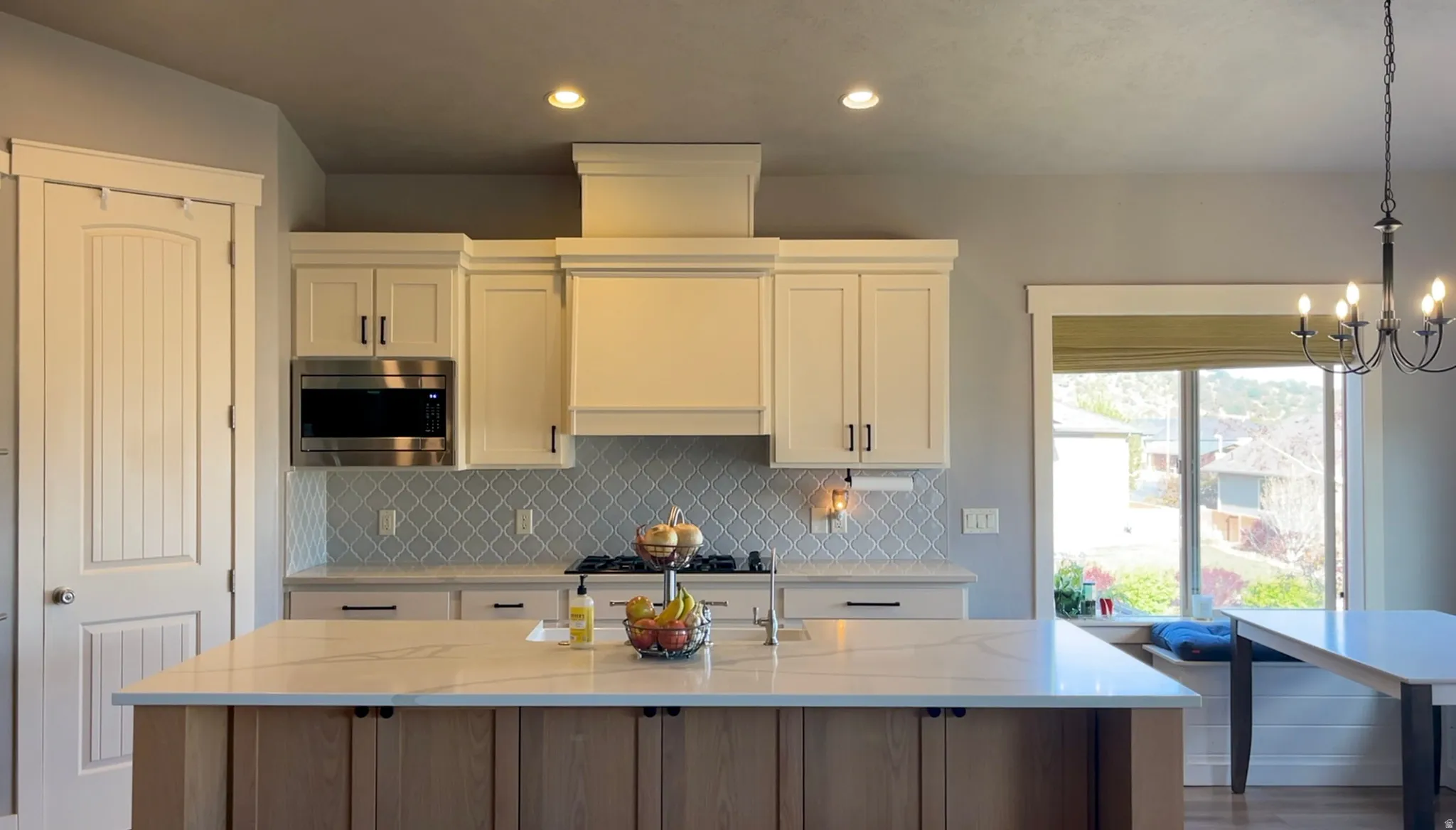 Two tone kitchen featuring light stone countertops, stainless steel microwave, decorative backsplash, a kitchen island with sink, and two tone color scheme