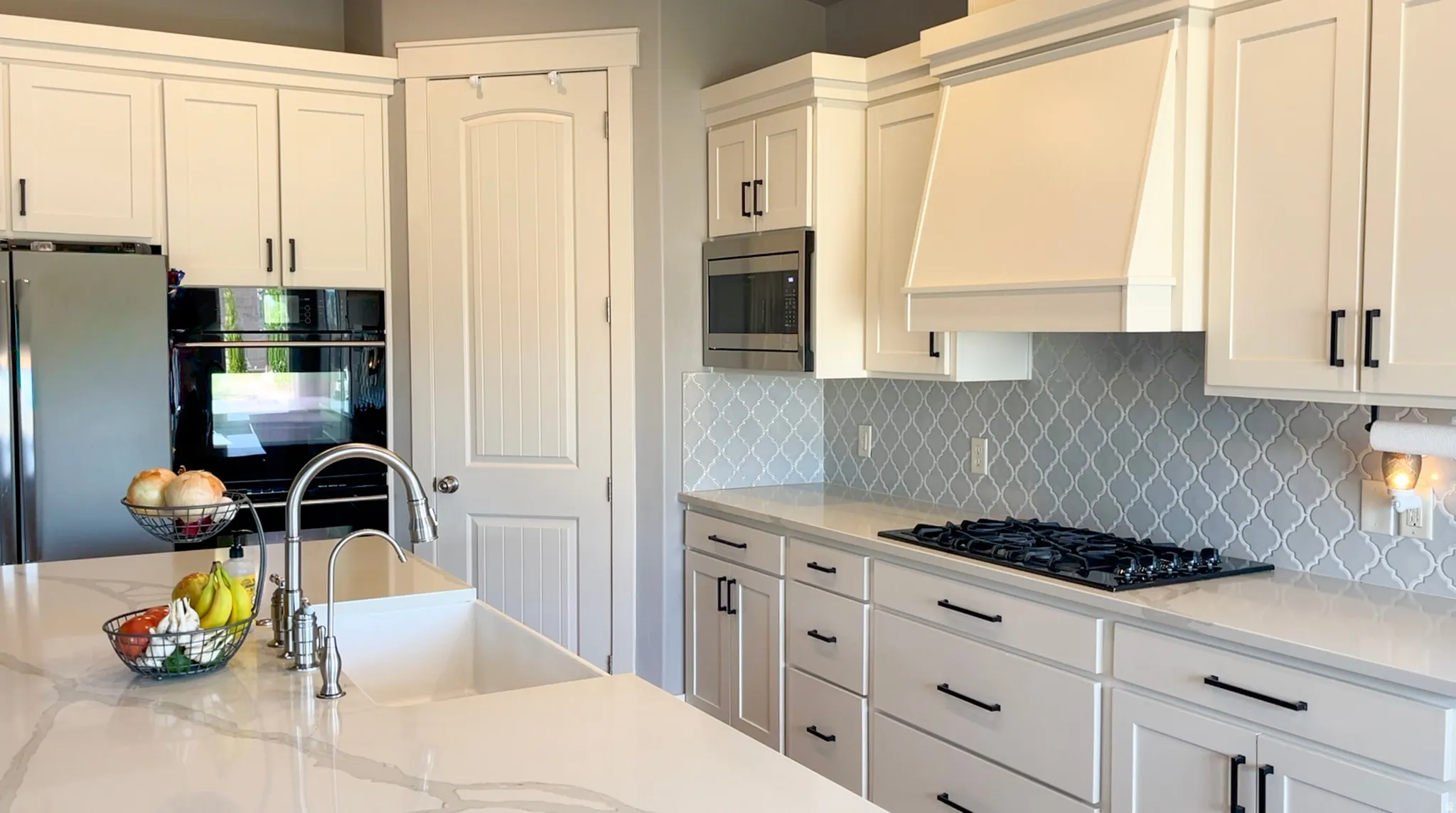 Kitchen featuring light stone counters, black appliances, backsplash, and white cabinets