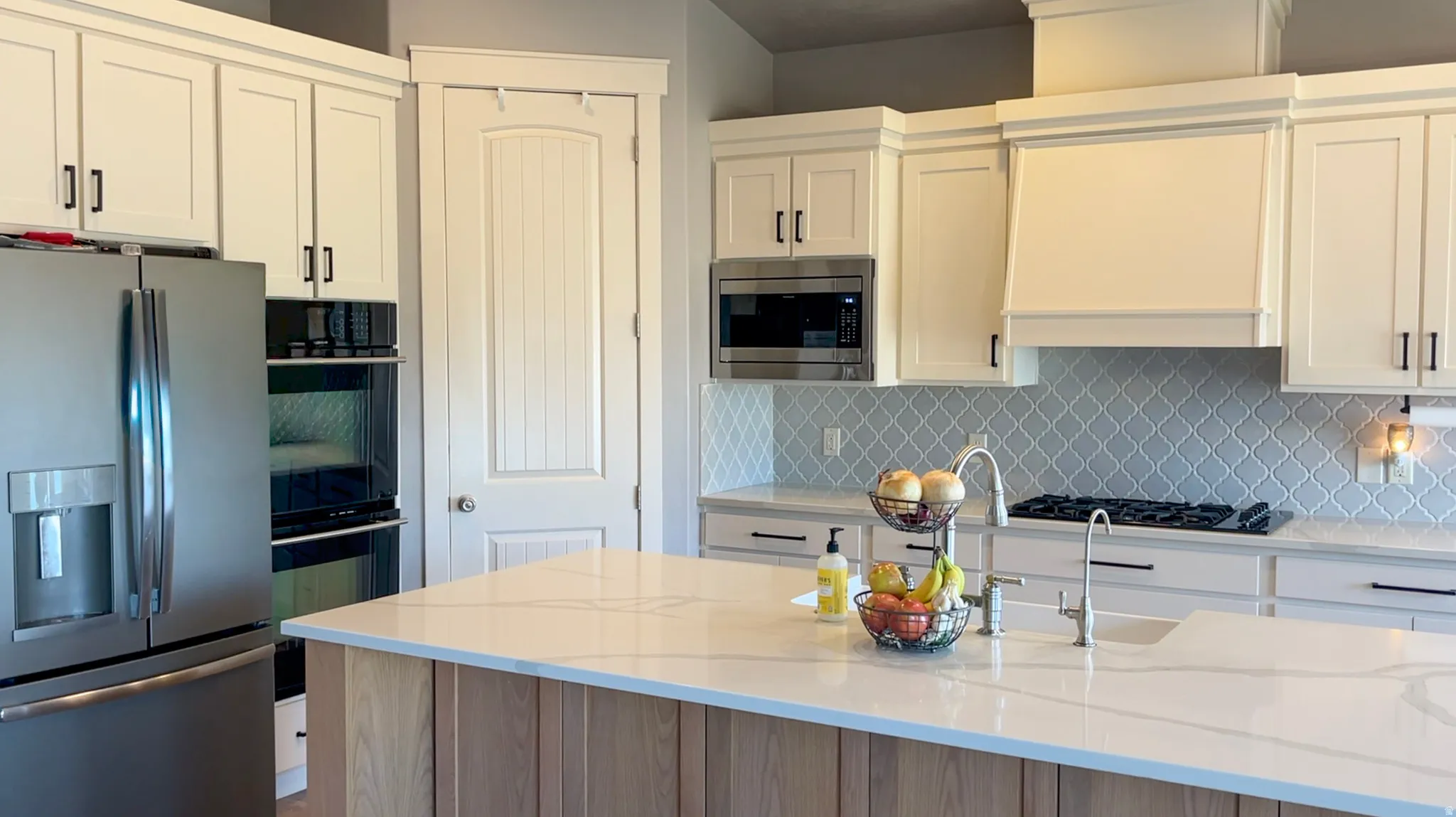 Kitchen featuring stainless steel appliances, light stone countertops, tasteful backsplash, and two tone cabinets
