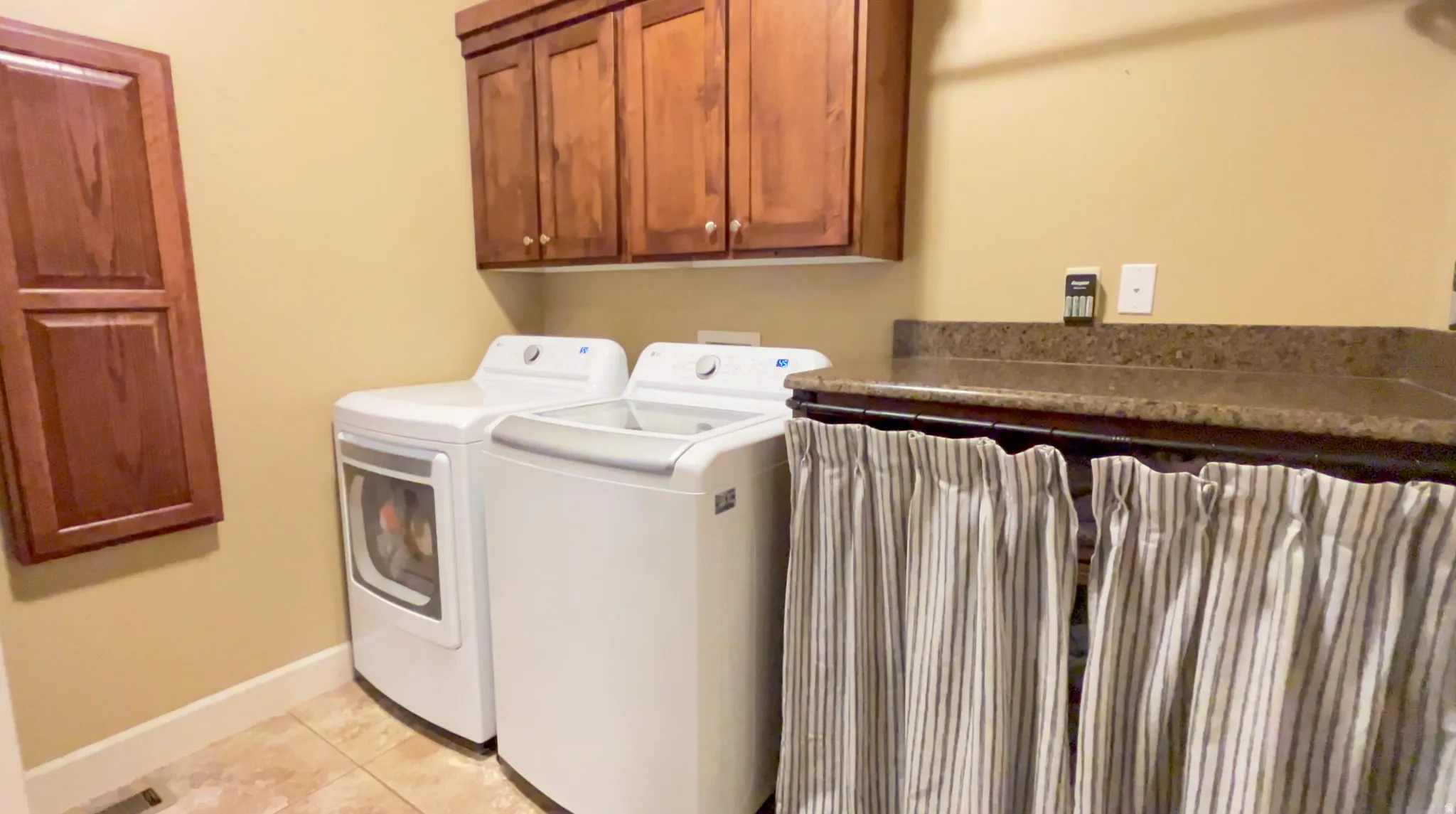Laundry area with independent washer and dryer, cabinet space, and light tile patterned floors