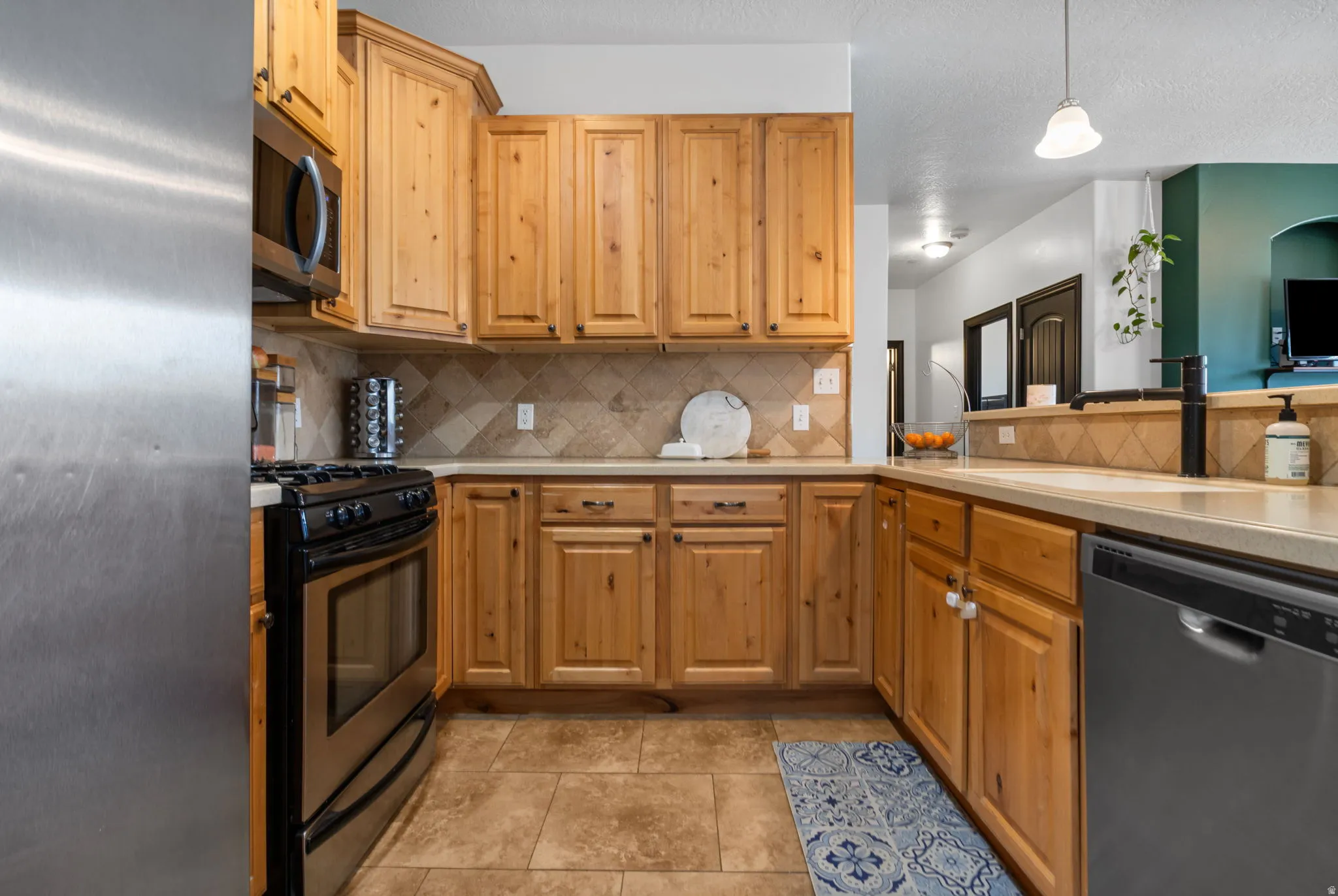 Kitchen featuring stanless steel appliances, light countertops, tasteful backsplash, decorative light fixtures, and light tile patterned floors