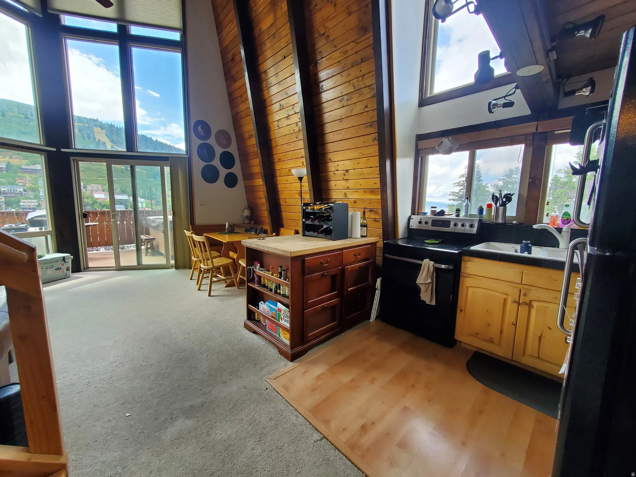 Kitchen with freestanding refrigerator, black range with electric stovetop, wood walls, light carpet, and light countertops
