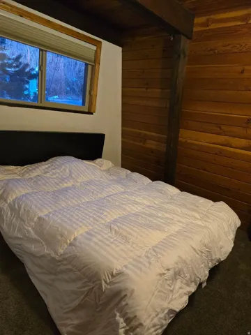 Carpeted bedroom with wood walls and beamed ceiling