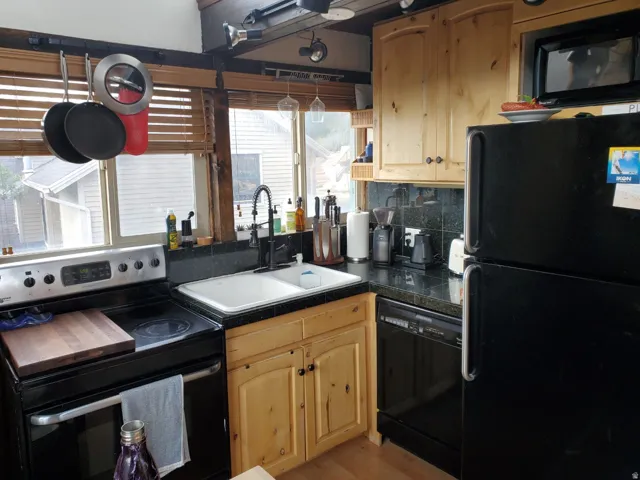 Kitchen with black appliances, light wood finish cabinets, tile countertops, and tasteful backsplash