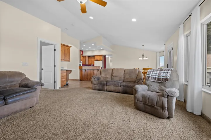 Living room with a ceiling fan, light carpet, lofted ceiling, and suspended lighting