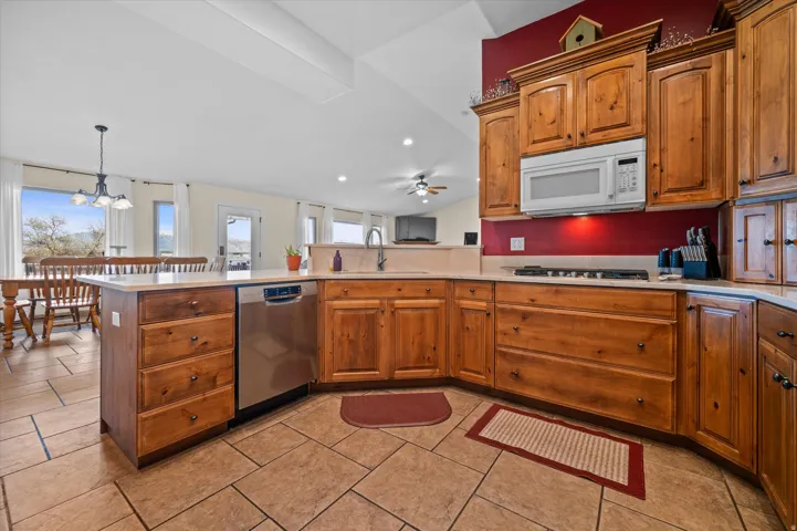 Kitchen featuring wood finish cabinetry, stainless steel dishwasher, white microwave, a peninsula, and vaulted ceiling