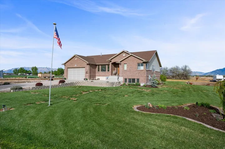 View of front of home featuring a mountain view, brick siding, a front lawn, a garage, and concrete driveway