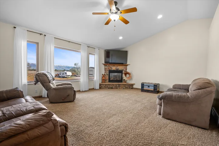 Living room with ceiling fan, carpet floors, lofted ceiling, recessed lighting, and a stone fireplace